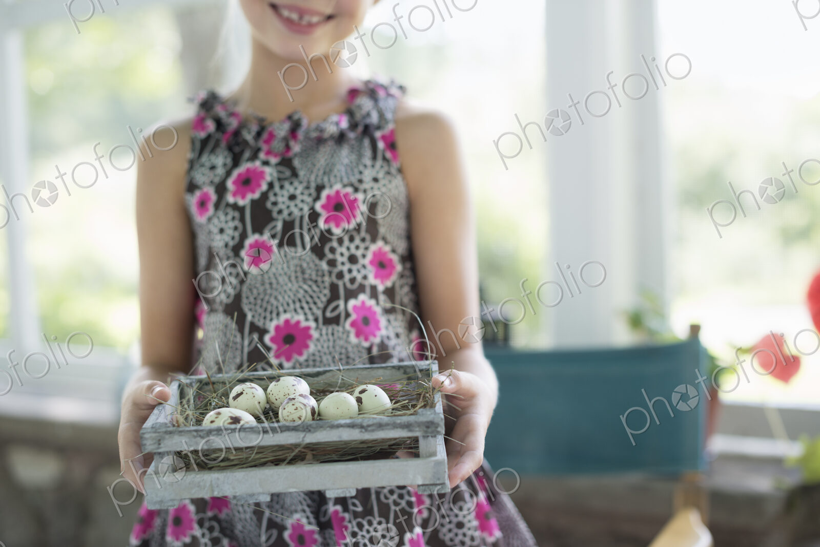 A young girl in a floral dress, examining a clutch of speckled bird eggs in a box.
