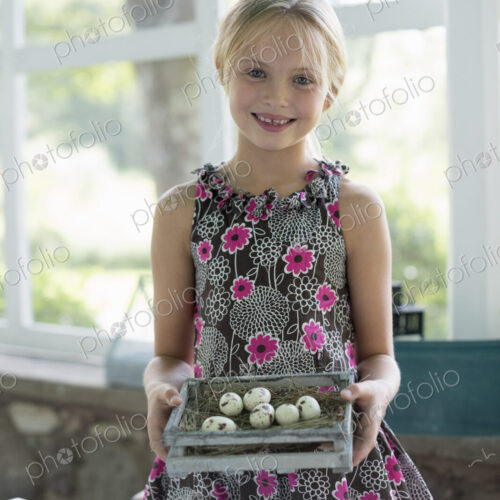 A young girl in a floral dress, examining a clutch of speckled bird eggs in a box. A young girl in a floral dress, examining a clutch of speckled bird eggs in a box.