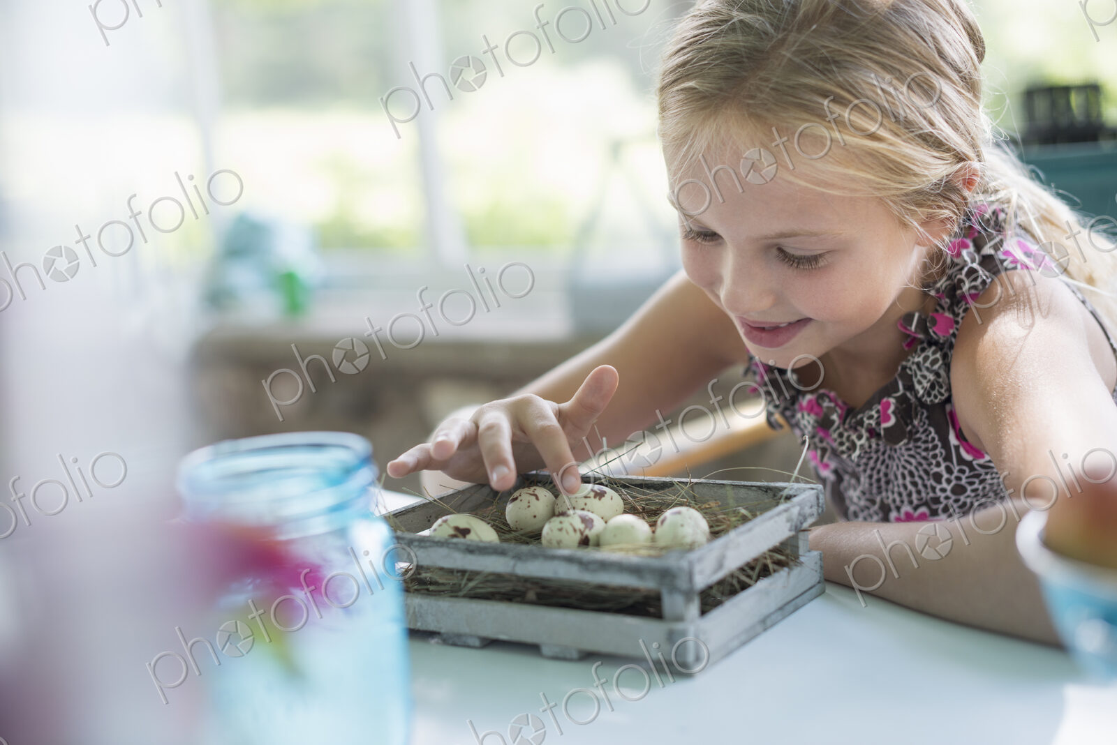 A young girl in a floral dress, examining a clutch of speckled bird eggs in a box.