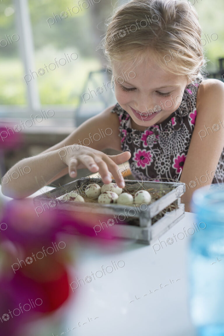 A young girl in a floral dress, examining a clutch of speckled bird eggs in a box.