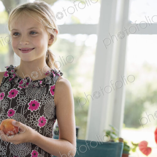 A young girl in a floral dress holding a peach fruit. A young girl in a floral dress holding a peach fruit.