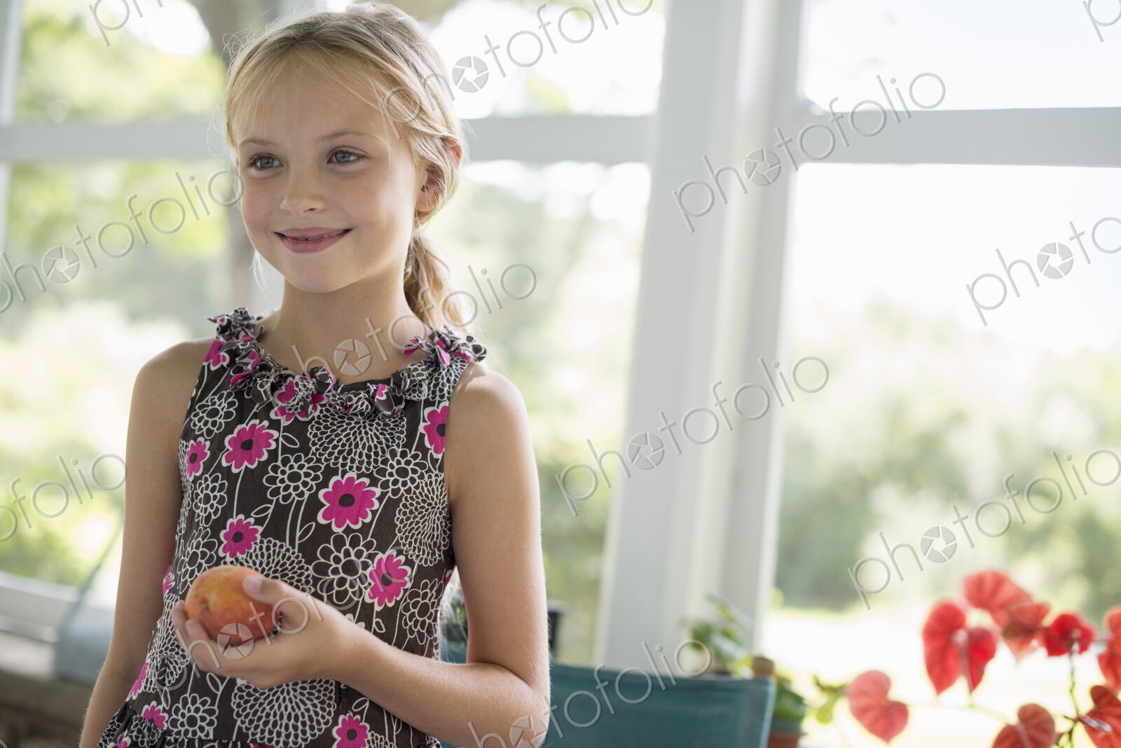 A young girl in a floral dress holding a peach fruit.