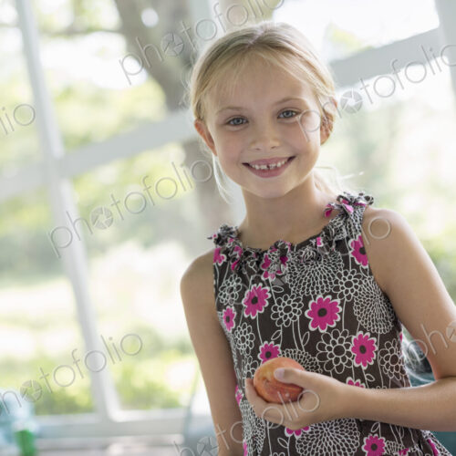 A young girl in a floral dress holding a peach fruit. A young girl in a floral dress holding a peach fruit.