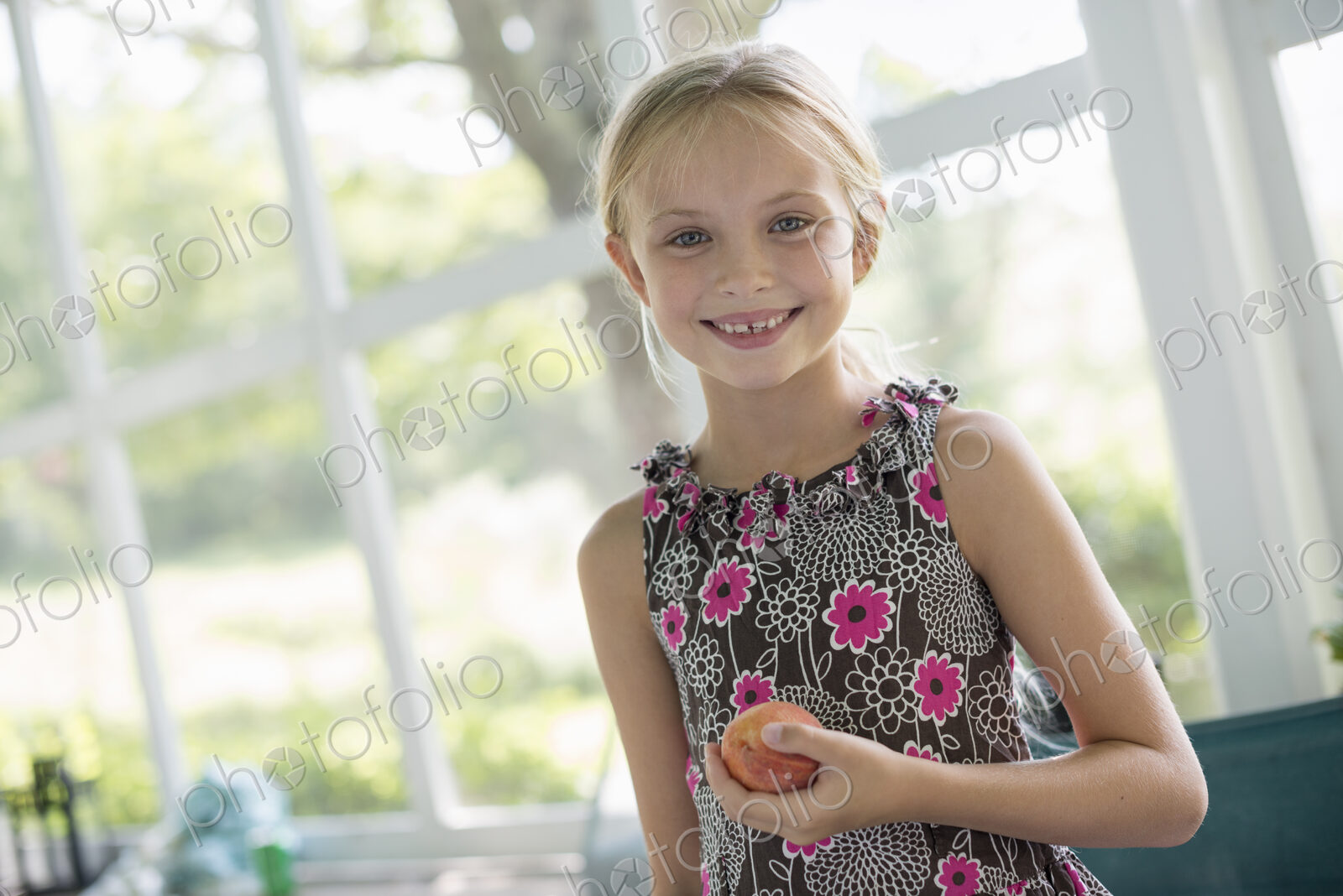 A young girl in a floral dress holding a peach fruit.