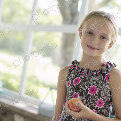 A young girl in a floral dress holding a peach fruit. A young girl in a floral dress holding a peach fruit.