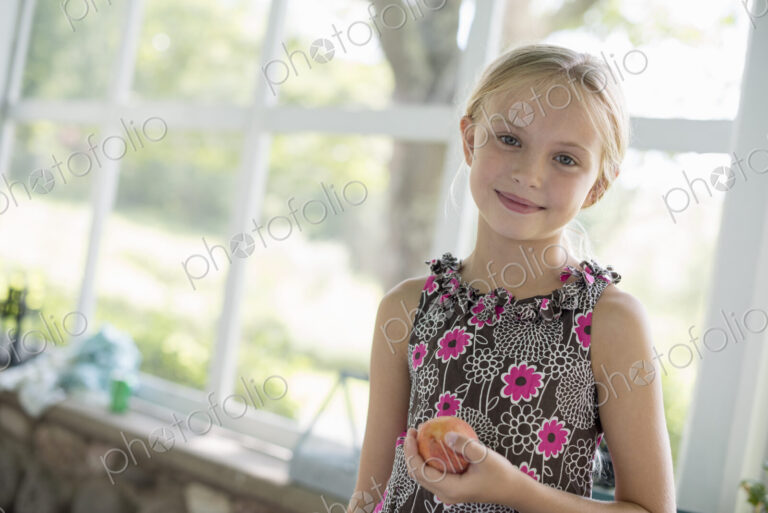 A young girl in a floral dress holding a peach fruit.