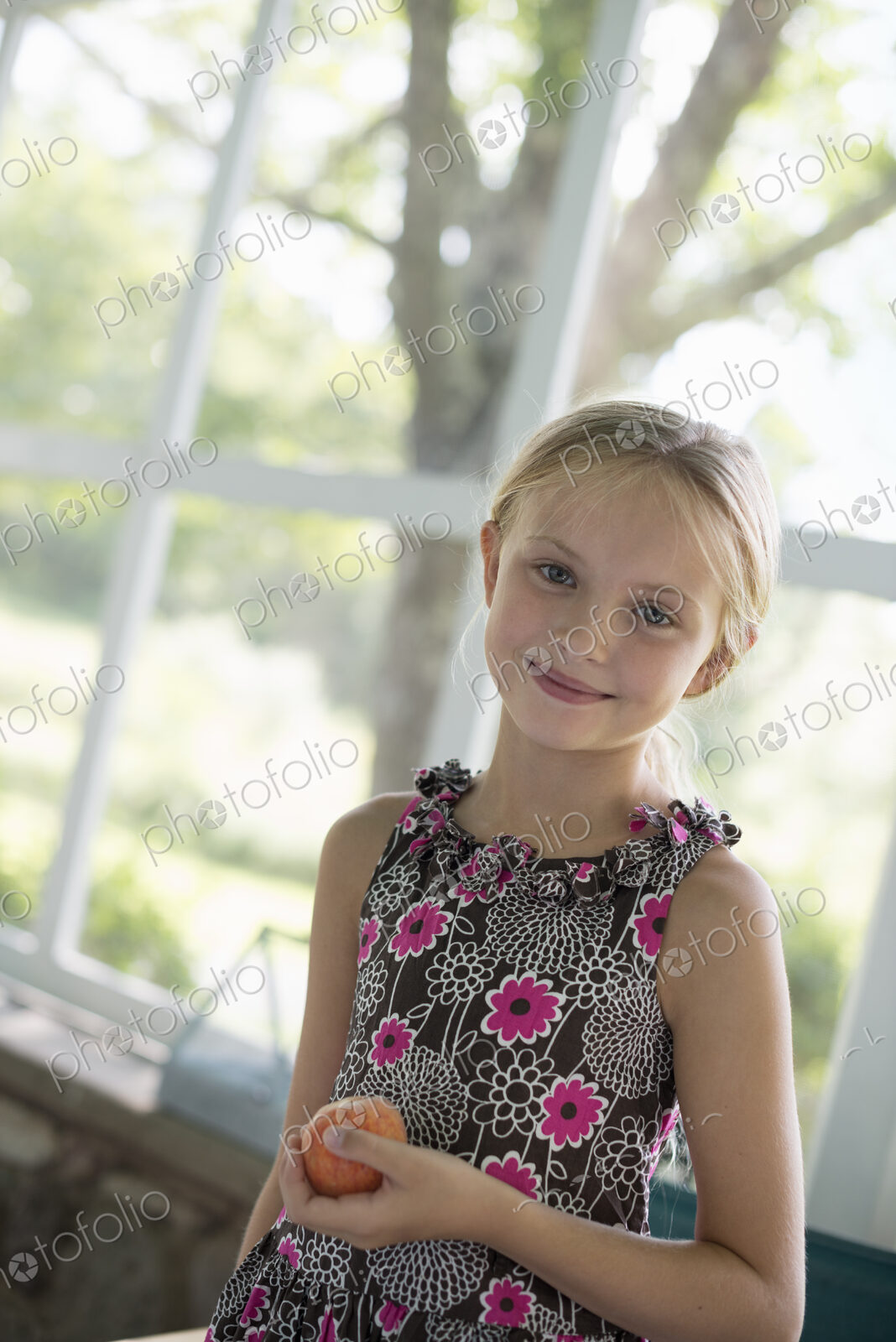 A young girl in a floral dress holding a peach fruit.