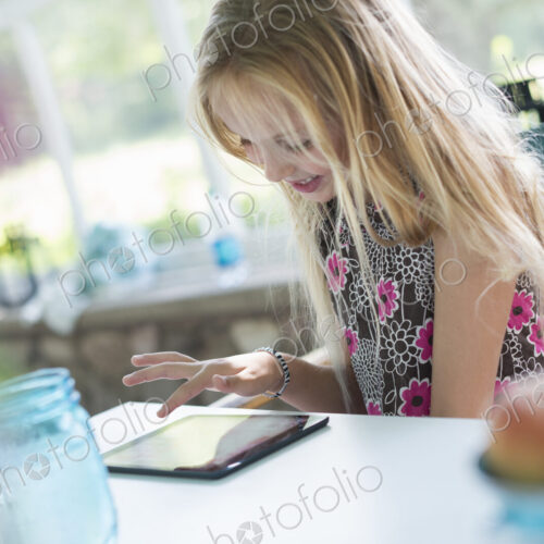 A young girl in a flowered dress using a digital tablet. Sitting at a table. A young girl in a flowered dress using a digital tablet. Sitting at a table.