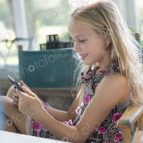 A young girl in a flowered dress using a digital tablet. Sitting at a table. A young girl in a flowered dress using a digital tablet. Sitting at a table.