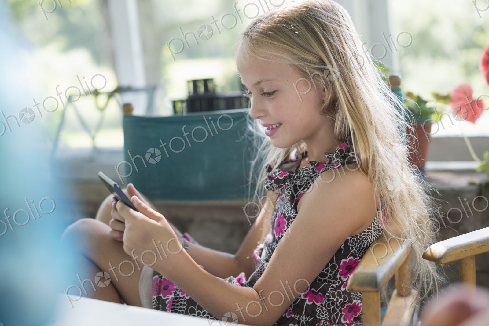A young girl in a flowered dress using a digital tablet. Sitting at a table.