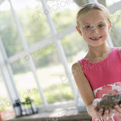 A young girl in a kitchen wearing a pink dress. Holding a bird;s nest. A young girl in a kitchen wearing a pink dress. Holding a bird;s nest.