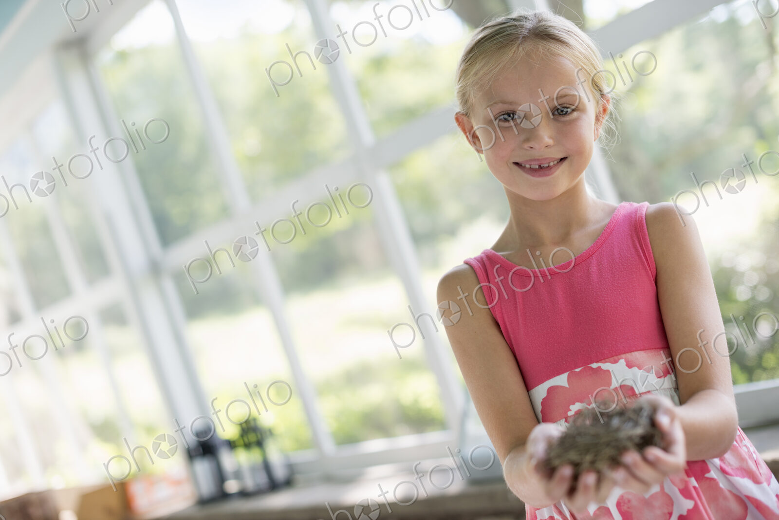 A young girl in a kitchen wearing a pink dress. Holding a bird;s nest.