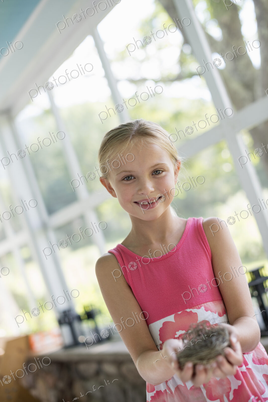 A young girl in a kitchen wearing a pink dress. Holding a bird;s nest.