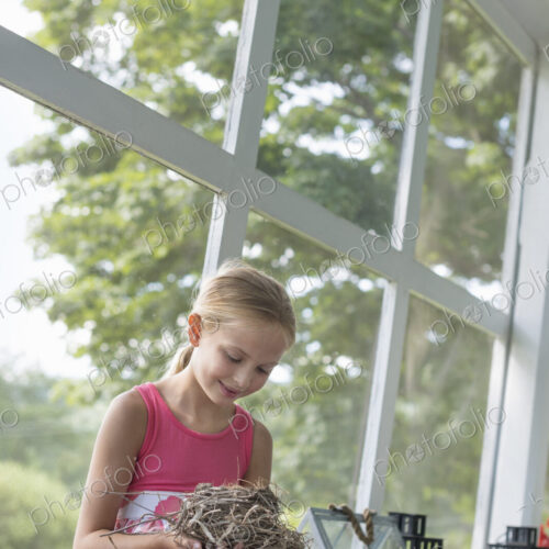 A young girl in a kitchen wearing a pink dress. Holding a bird;s nest. A young girl in a kitchen wearing a pink dress. Holding a bird;s nest.