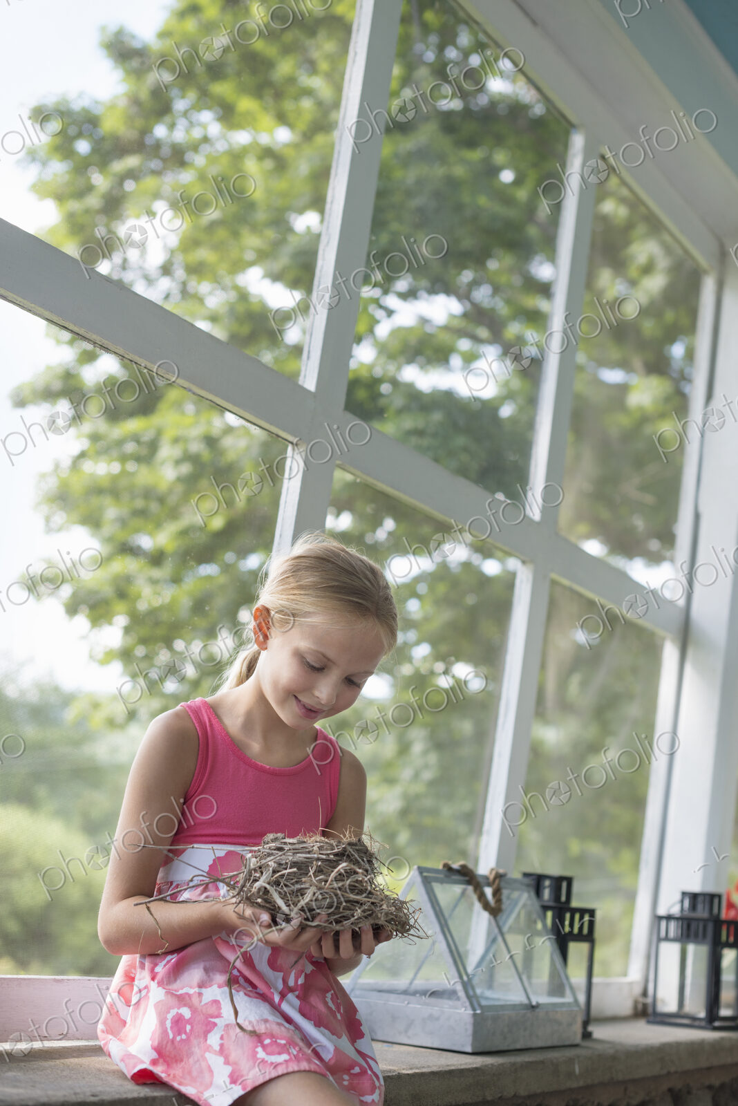 A young girl in a kitchen wearing a pink dress. Holding a bird;s nest.