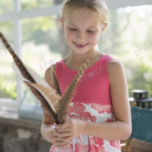A young girl in a kitchen wearing a pink dress. Holding a bunch of bird feathers. A young girl in a kitchen wearing a pink dress. Holding a bunch of bird feathers.