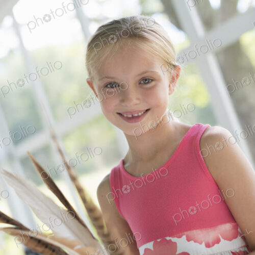 A young girl in a kitchen wearing a pink dress. Holding a bunch of bird feathers. A young girl in a kitchen wearing a pink dress. Holding a bunch of bird feathers.
