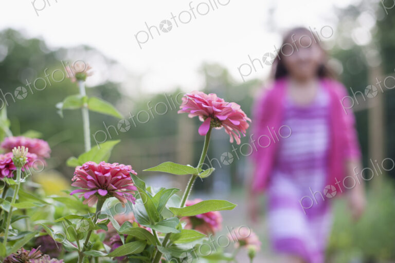 A young girl in a pink dress, walking past a bed of flowers in an organic garden.