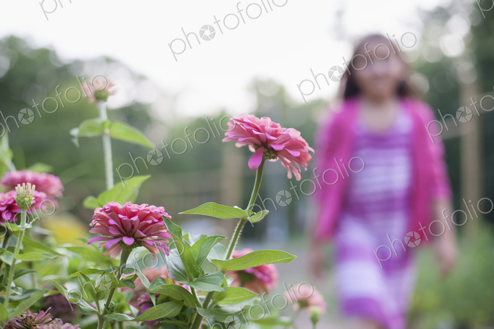 A young girl in a pink dress, walking past a bed of flowers in an organic garden.