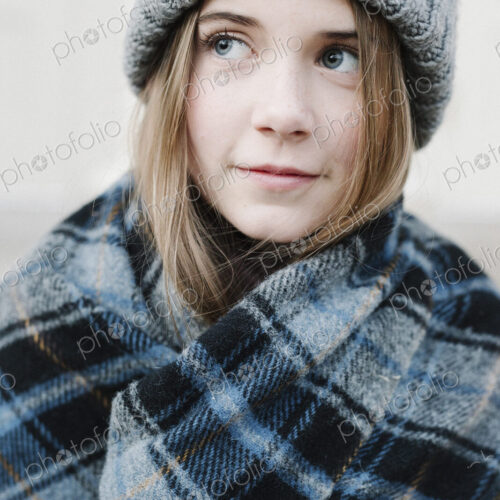 A young girl in a tartan plaid shawl and woolly hat outdoors in the winter.