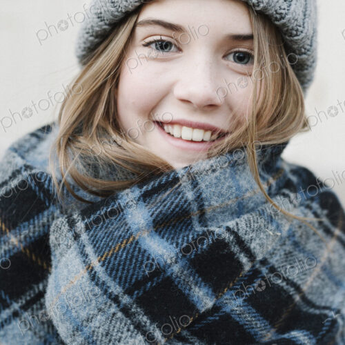 A young girl in a tartan plaid shawl and woolly hat outdoors in the winter.
