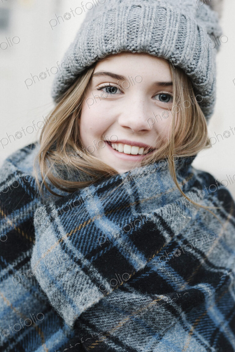 A young girl in a tartan plaid shawl and woolly hat outdoors in the winter.