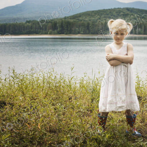 A young girl in a white summer dress, standing with her arms folded looking at the camera. A young girl in a white summer dress, standing with her arms folded looking at the camera.