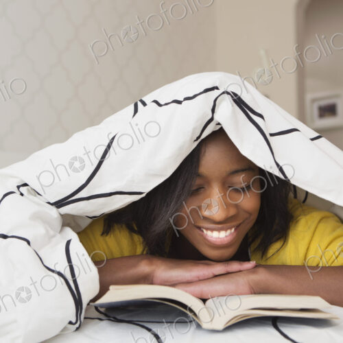 A young girl in her bed, under a duvet reading a book. A young girl in her bed, under a duvet reading a book.
