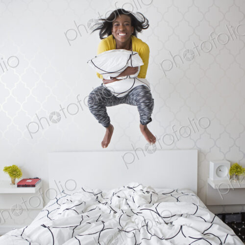 A young girl jumping high in the air above her bed.
