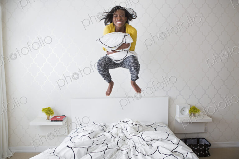 A young girl jumping high in the air above her bed.