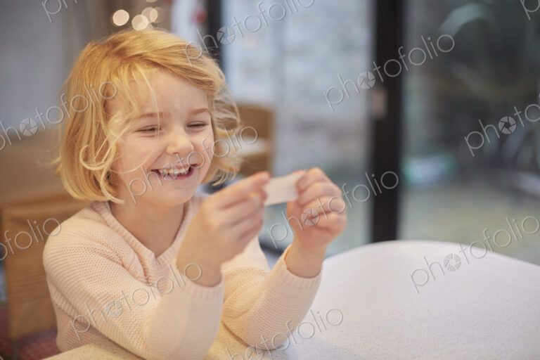 A young girl laughing and looking at a small piece of paper, a joke from a Christmas…
