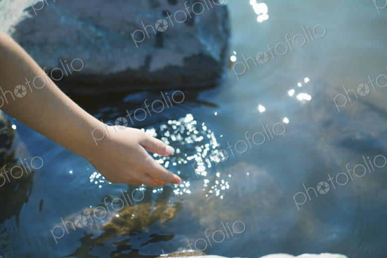A young girl leaning forward to put her hand into clear shallow lake water.