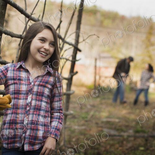 A young girl leaning on a fence, and two people in the background. An organic farm. A young girl leaning on a fence, and two people in the background. An organic farm.