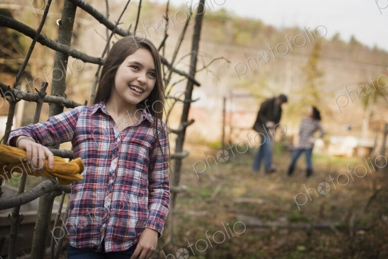 A young girl leaning on a fence, and two people in the background. An organic farm.