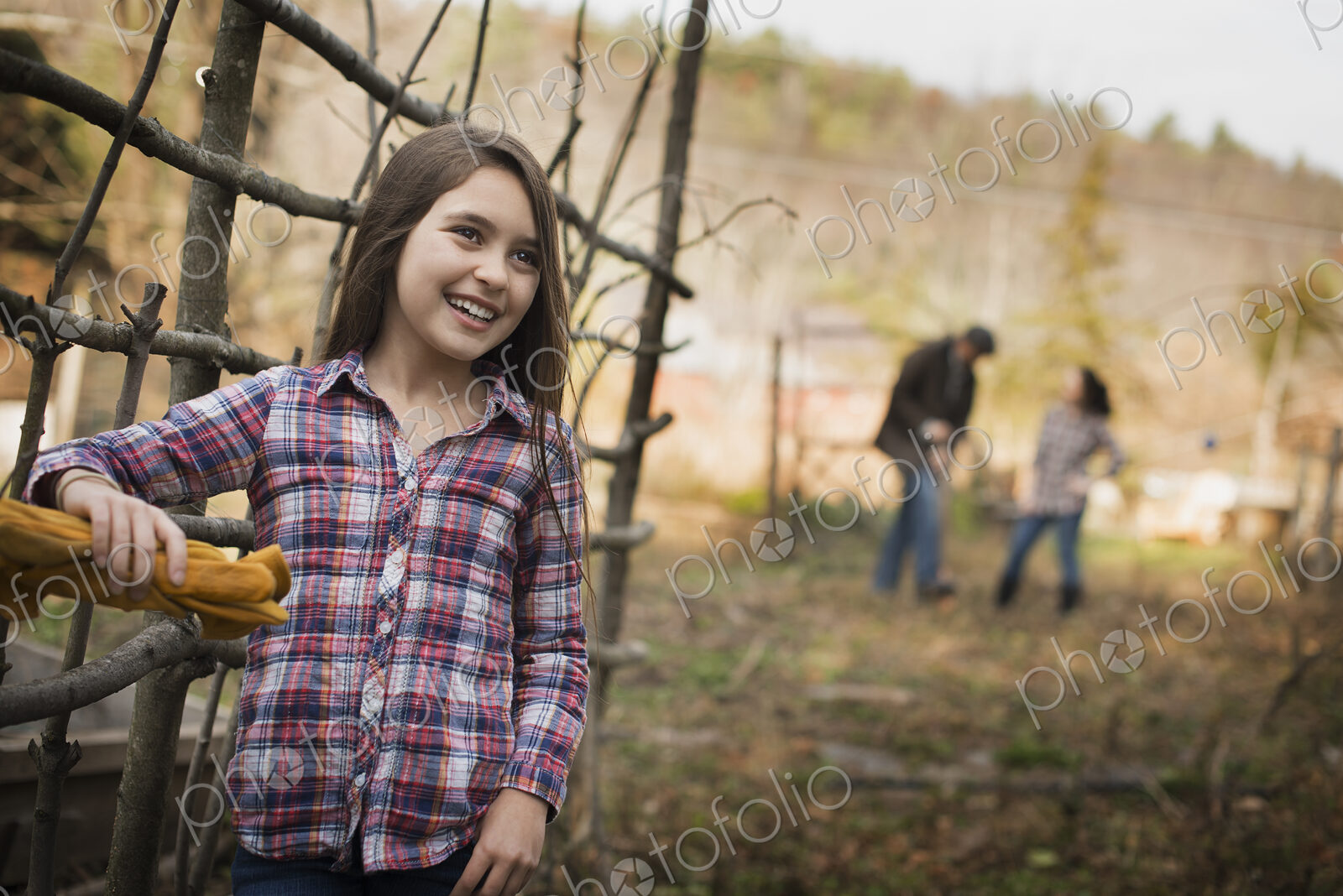 A young girl leaning on a fence, and two people in the background. An organic farm.