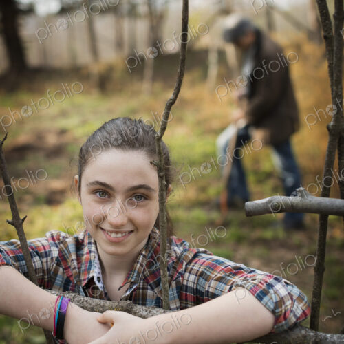 A young girl leaning on a fence, on an organic farm. A man digging the soil in the… A young girl leaning on a fence, on an organic farm. A man digging the soil in the…