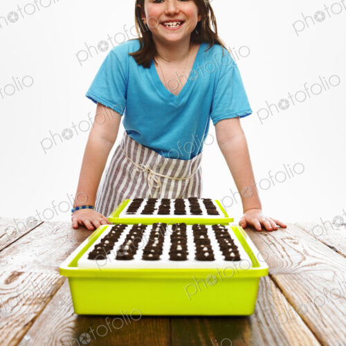A young girl leaning on a table with two tray of freshly planted seeds resting on dark… A young girl leaning on a table with two tray of freshly planted seeds resting on dark…