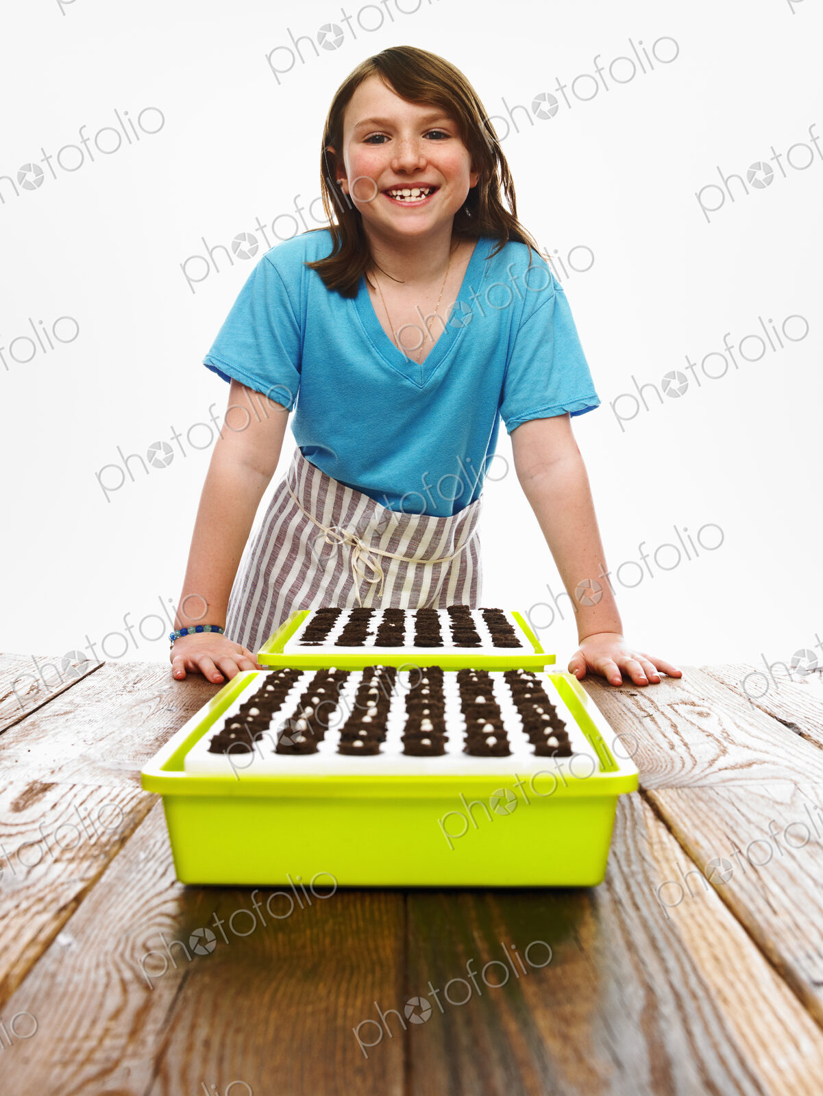 A young girl leaning on a table with two tray of freshly planted seeds resting on dark…