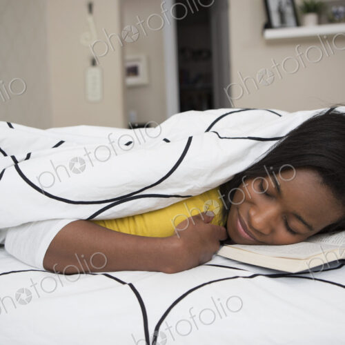 A young girl lying in her bed with her face resting on an open bok.