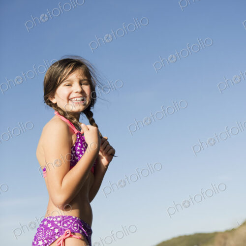 A young girl on a jetty with paddleboarders in the background.