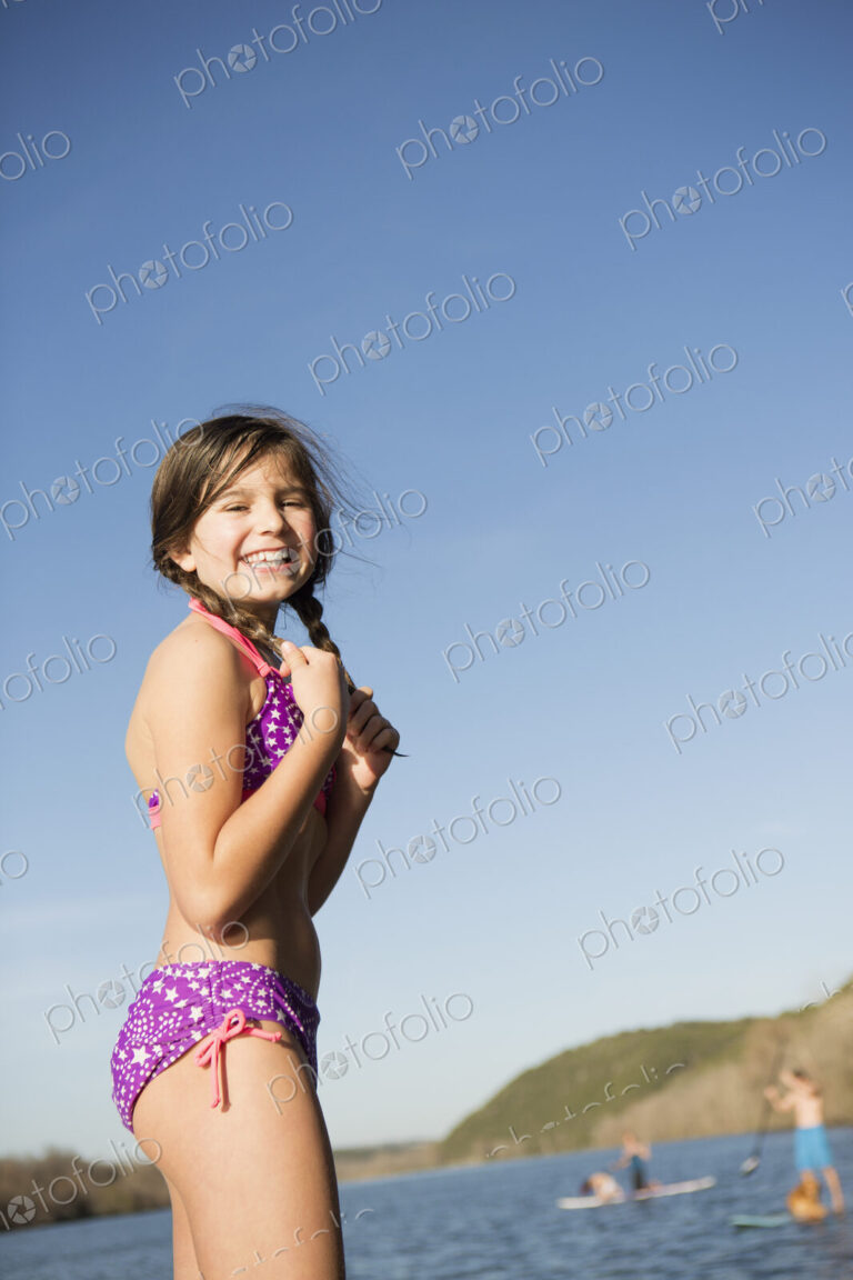 A young girl on a jetty with paddleboarders in the background.