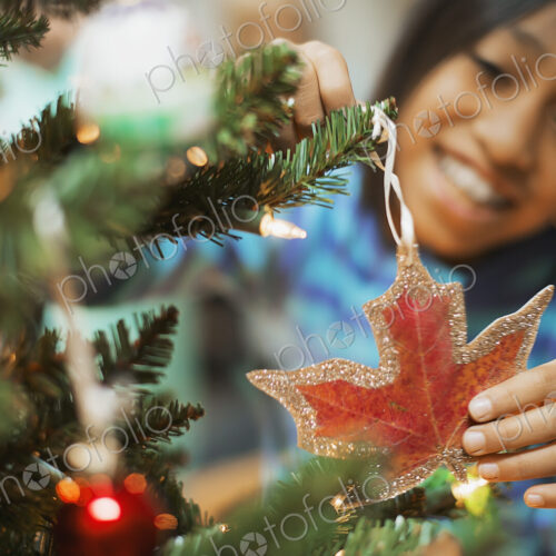 A young girl placing a handmade Christmas ornament in the sha pe of a maple leaf on a… A young girl placing a handmade Christmas ornament in the sha pe of a maple leaf on a…