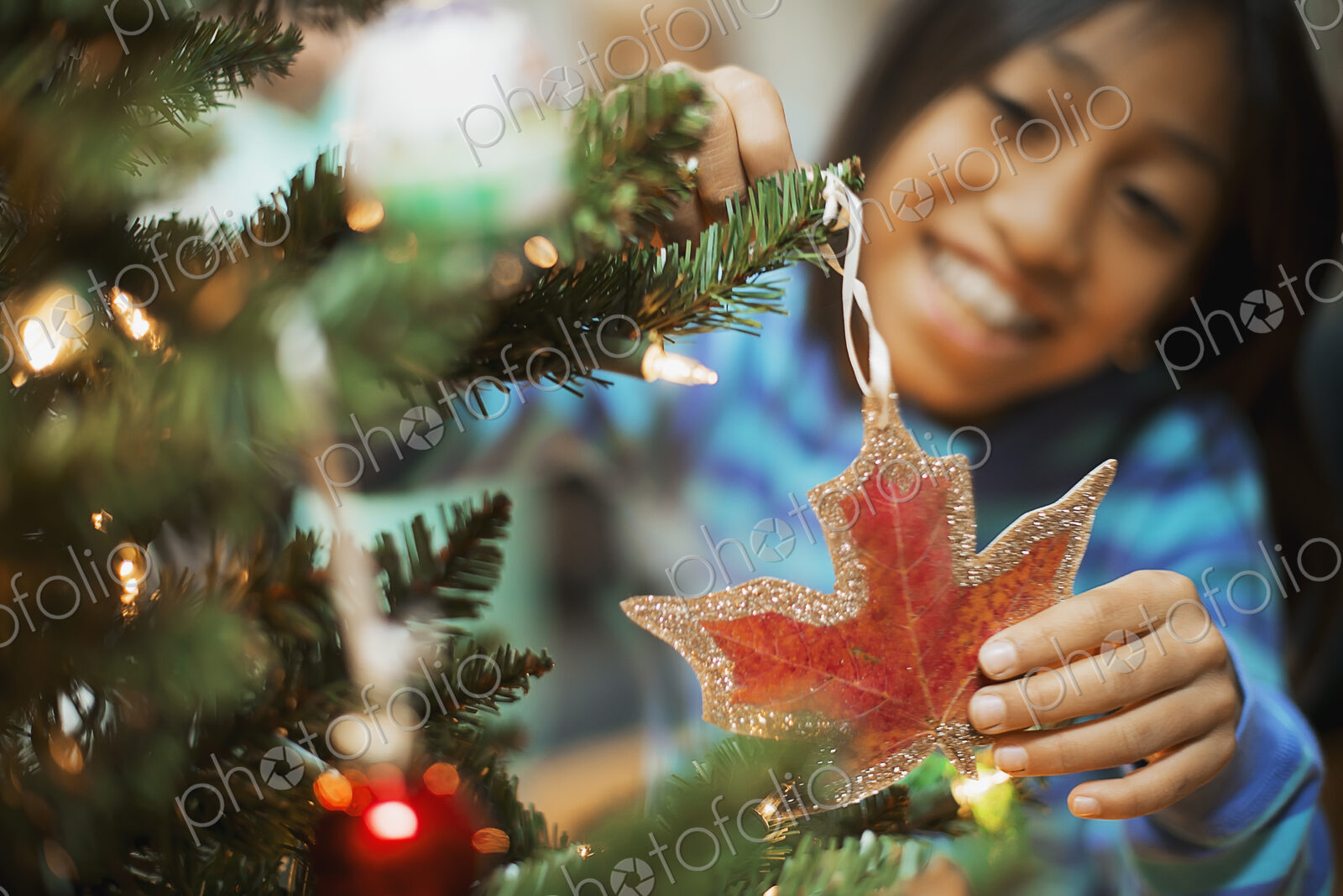 A young girl placing a handmade Christmas ornament in the sha pe of a maple leaf on a…