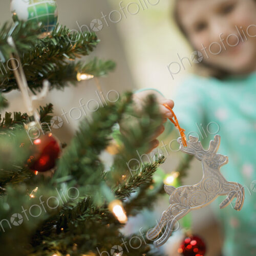 A young girl placing a homemade Christmas ornament on a tree.