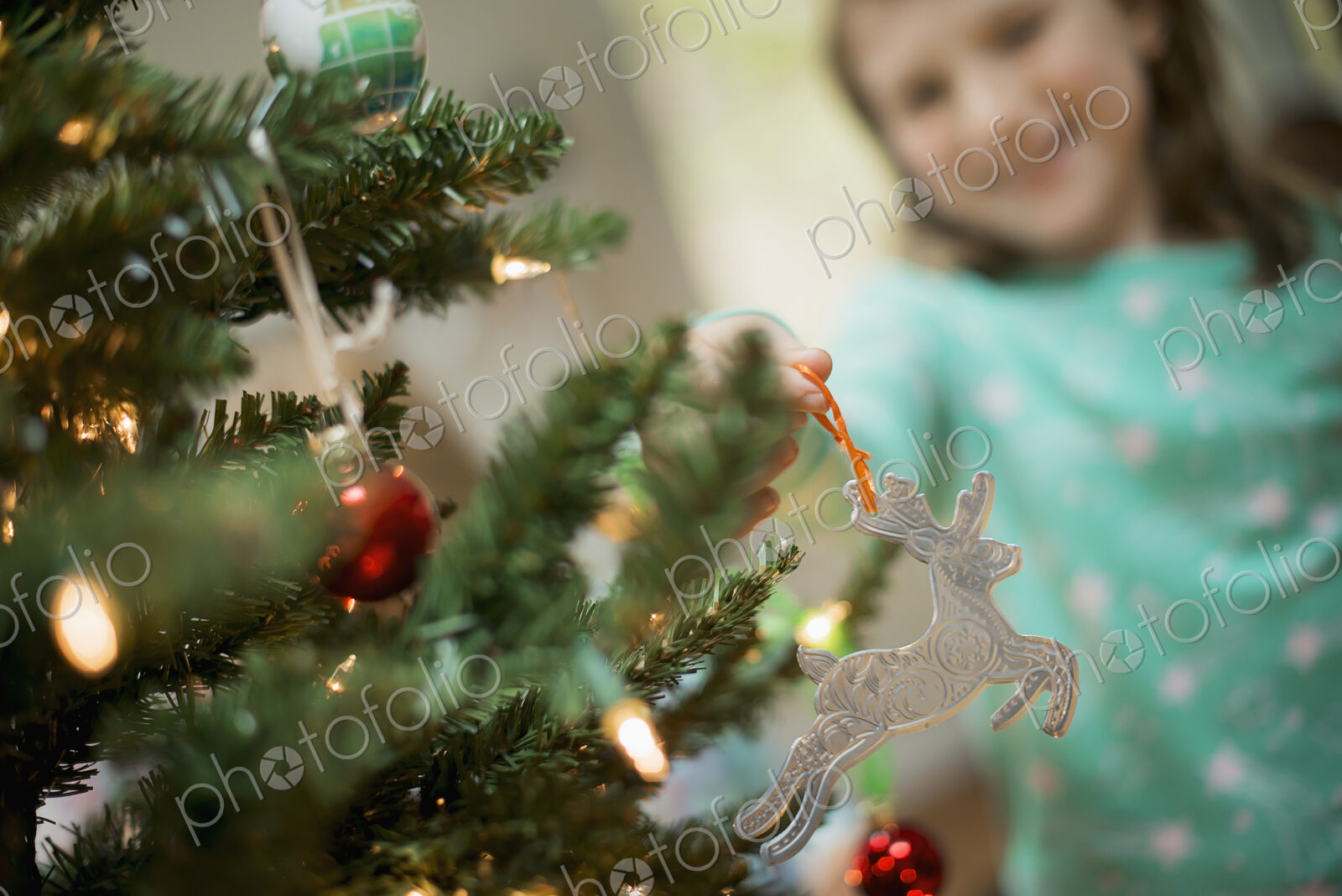 A young girl placing a homemade Christmas ornament on a tree.