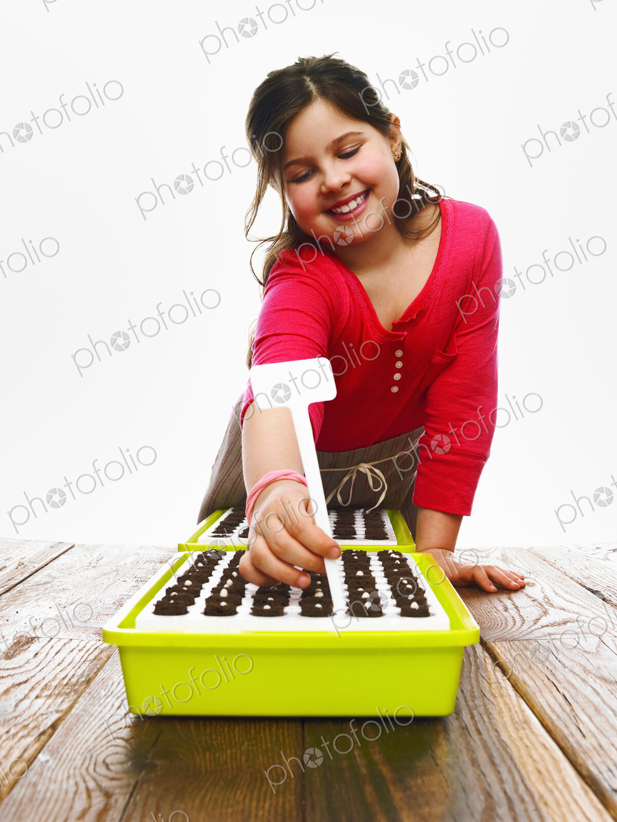 A young girl planting seeds in a modular seed tray with dark organic soil.