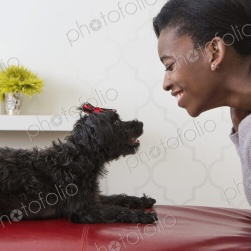 A young girl playing with her small black pet dog.