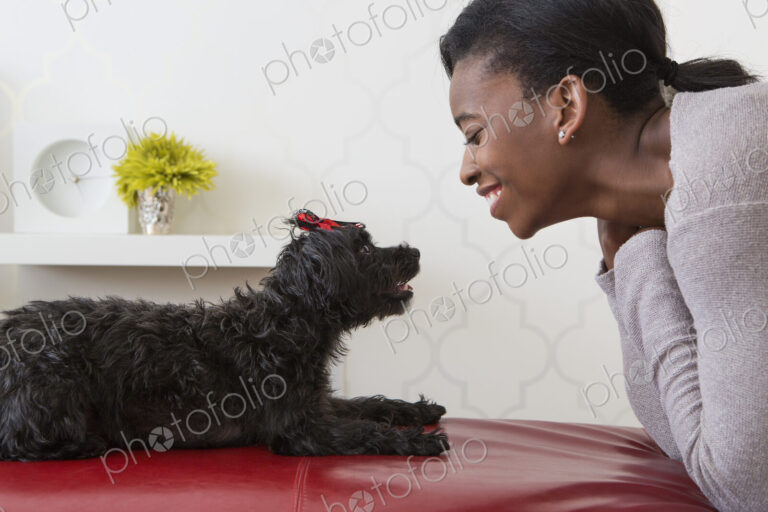 A young girl playing with her small black pet dog.