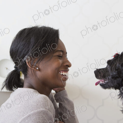 A young girl playing with her small black pet dog.