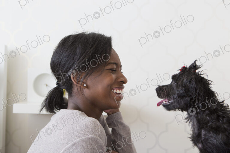 A young girl playing with her small black pet dog.